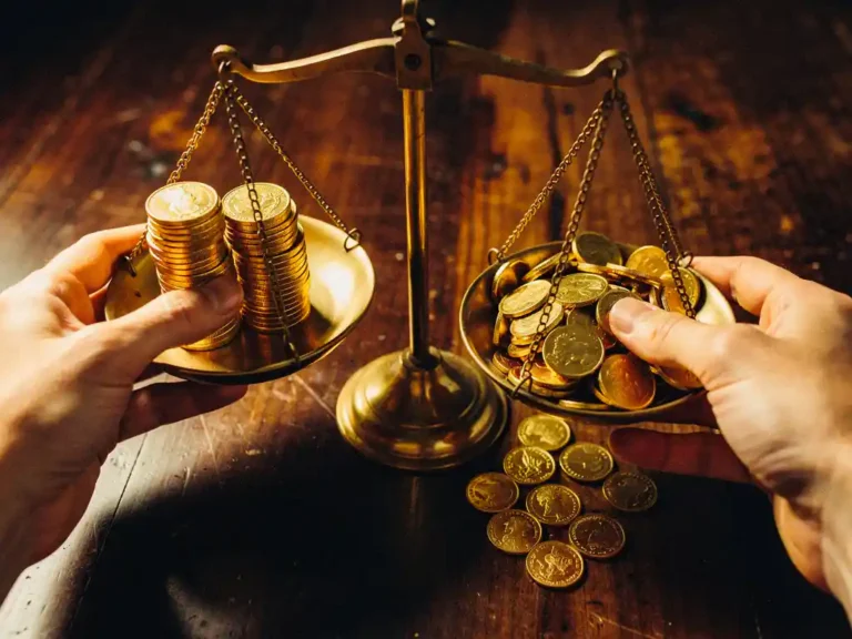 Handen wegen glimmende gouden munten op vintage messing weegschaal, munten vallen op donkere houten tafel